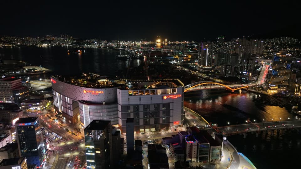 Aerial night view of Busan, South Korea featuring Lotte Mall and iconic bridges.