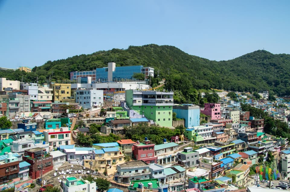 A vibrant aerial view of Busan's Gamcheon Culture Village with colorful houses and lush hills.