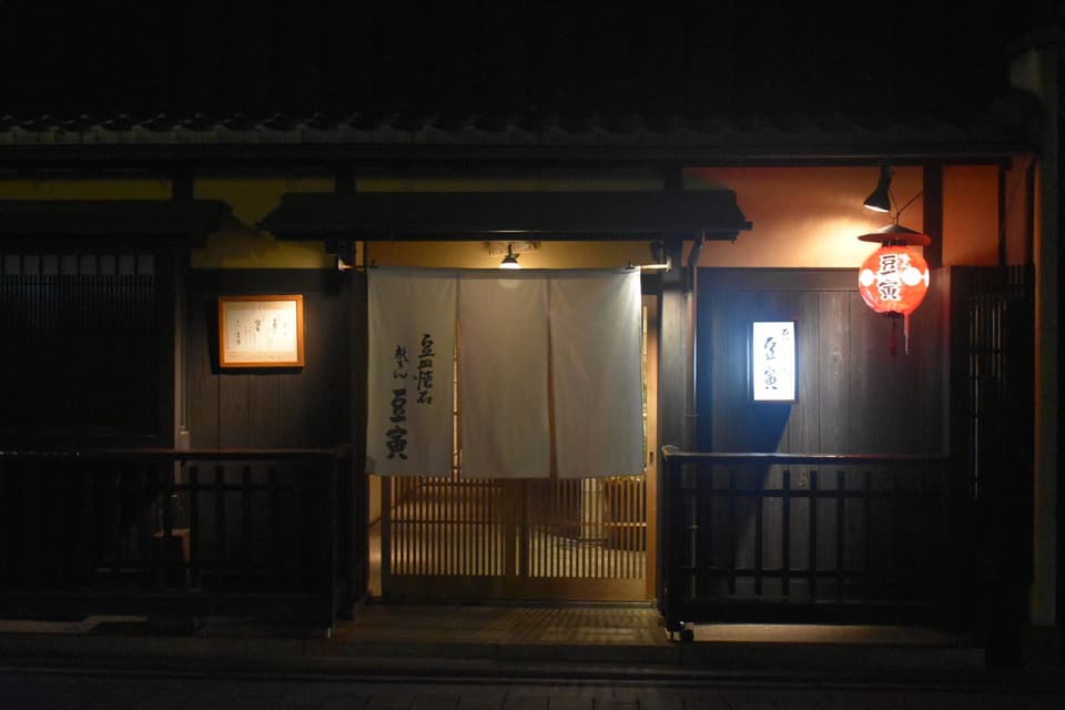 Nighttime view of a traditional Japanese restaurant entrance in Kyoto with lanterns and signage.