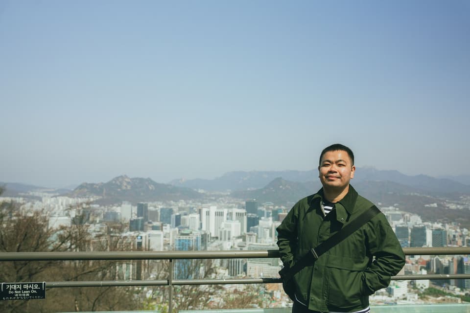 A man standing in front of the panoramic skyline of Seoul, South Korea on a clear day.