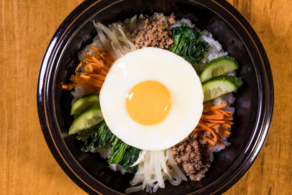Close-up of Korean Bibimbap with egg, rice, and fresh vegetables presented in a bowl.