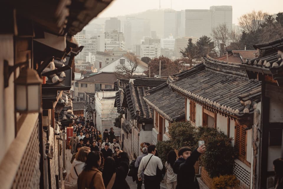 Explore the vibrant atmosphere of Bukchon Hanok Village in Seoul as tourists stroll past traditional Korean architecture.