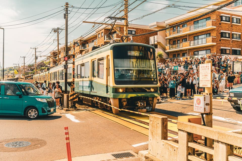 Vibrant street scene in Kamakura, Japan, showcasing a train crossing bustling streets filled with onlookers.