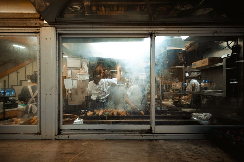 Chefs preparing food in a smokey kitchen at a Tokyo street food restaurant.