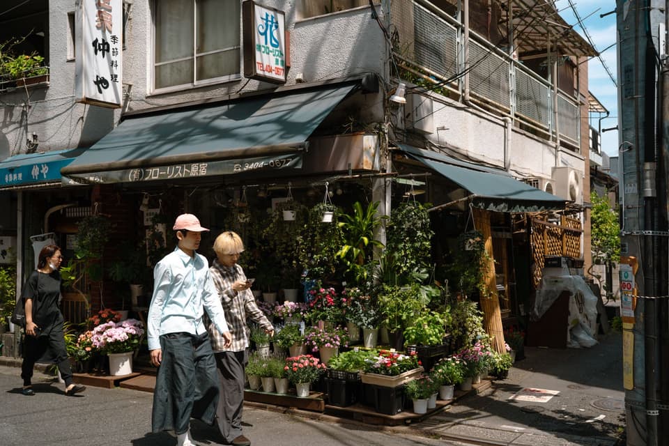 Charming florist shop in Tokyo's streets with pedestrians passing by, captured in daylight.