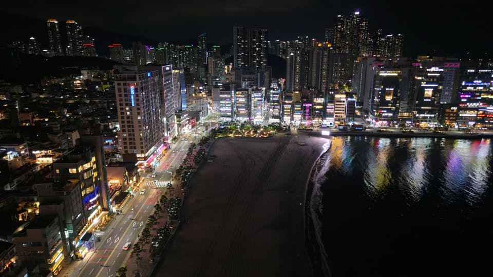 Aerial night view of Busan's illuminated skyline adjacent to the waterfront in South Korea.