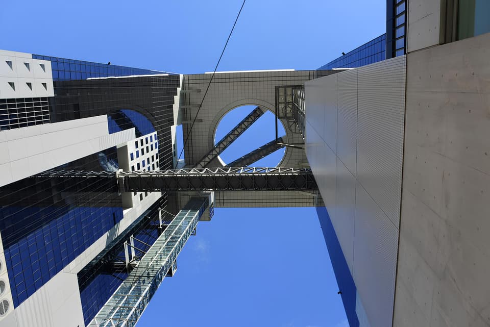 Dramatic upward angle of the Umeda Sky Building's sky bridge in Osaka, Japan against a clear blue sky.
