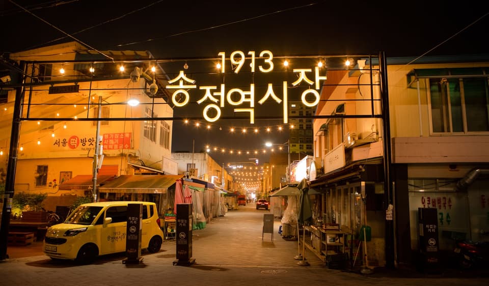 Illuminated entrance of 1913 Songjeong Market in Gwangju at night, showcasing vibrant street life and lively atmosphere.