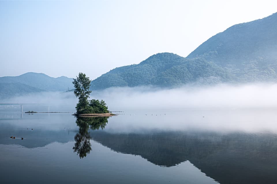 Serene island reflection in a misty lake with mountains, captured in Gapyeong, South Korea.