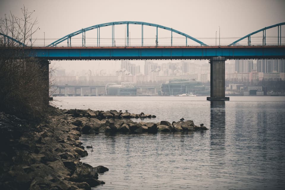 Scenic view of a blue bridge over the Han River with Seoul's cityscape in the background.