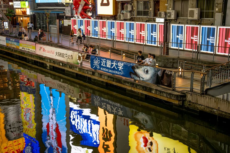 Colorful billboards reflecting in Dotonbori canal, a lively street scene in Osaka, Japan.