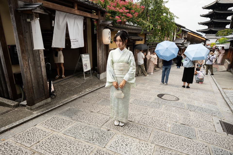 A woman in a kimono stands on a traditional Kyoto street with pagoda in the background.