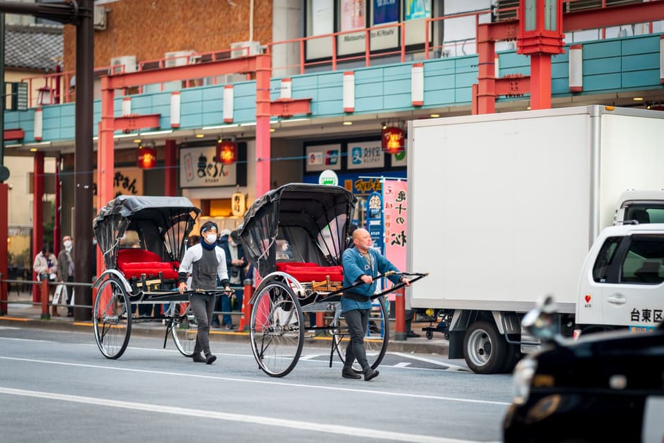 Two rickshaw drivers in traditional attire pulling rickshaws in bustling Asakusa, Tokyo.