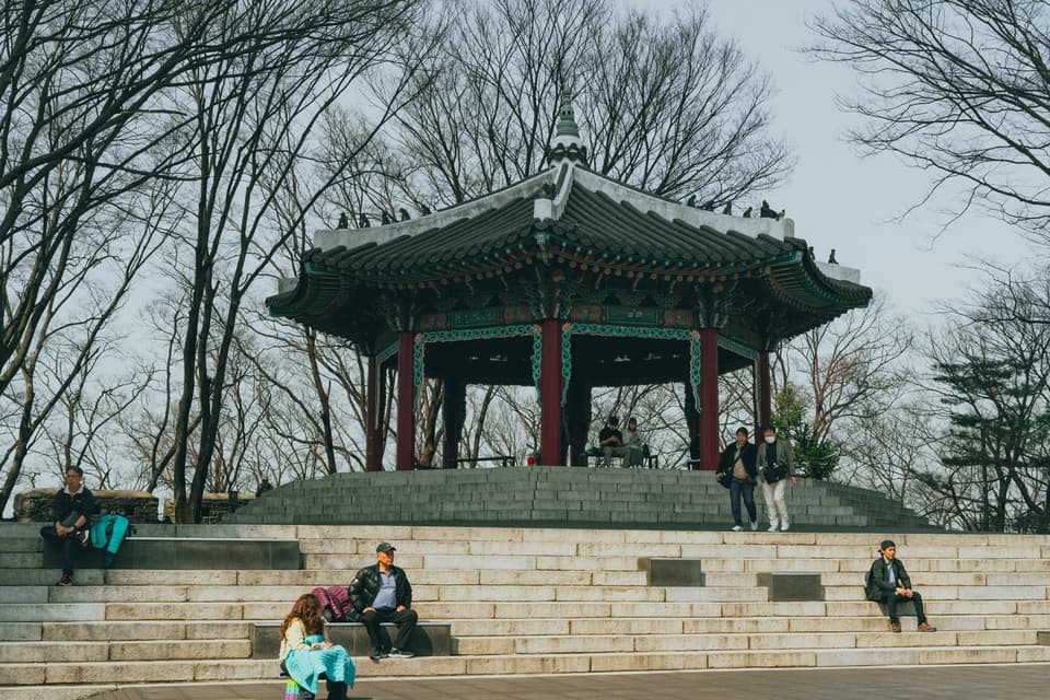 A serene scene of locals enjoying the picturesque traditional pavilion at Namsan Park in Seoul during spring.