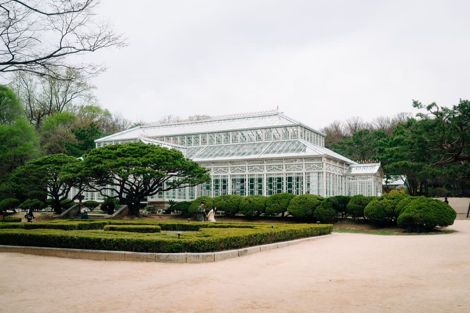 Elegant glass conservatory surrounded by lush greenery in a tranquil park in Seoul, South Korea.