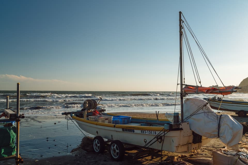 Fishing boats rest on Kamakura beach, Japan during a sunny day, capturing coastal life.