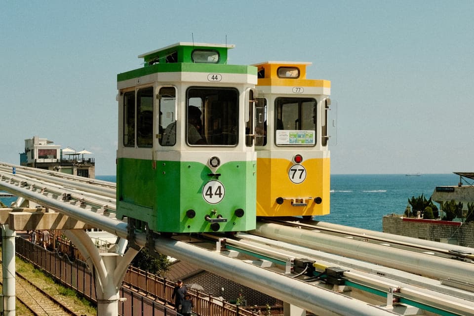 Vibrant monorail crossing over serene waters in Busan, South Korea.