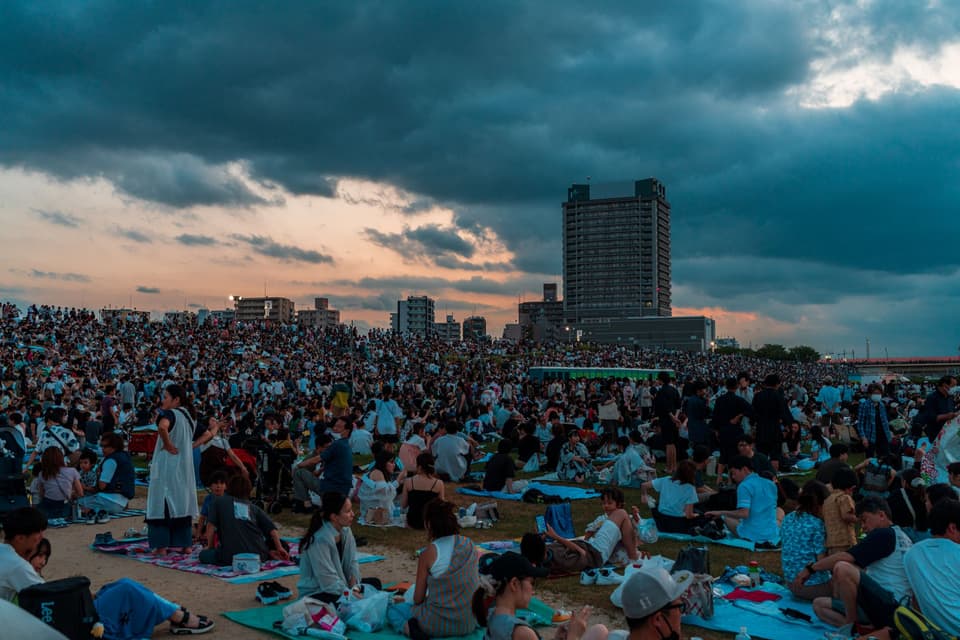 Large crowd attending a summer festival in Tokyo, Japan, under dramatic evening skies.