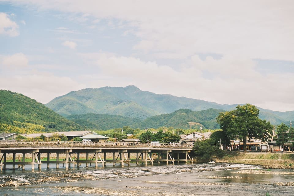 Discover the serene landscape of Arashiyama with its picturesque bridge and lush green mountains in Kyoto, Japan.