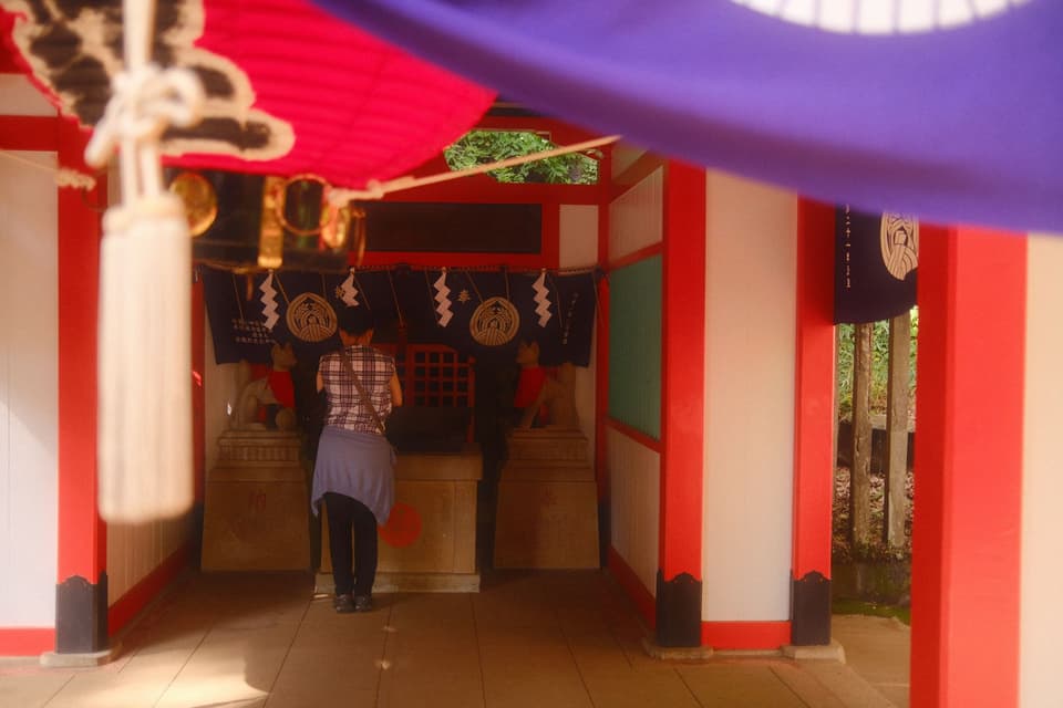 A person worships at a traditional shrine in Tokyo, Japan, featuring vibrant decor.